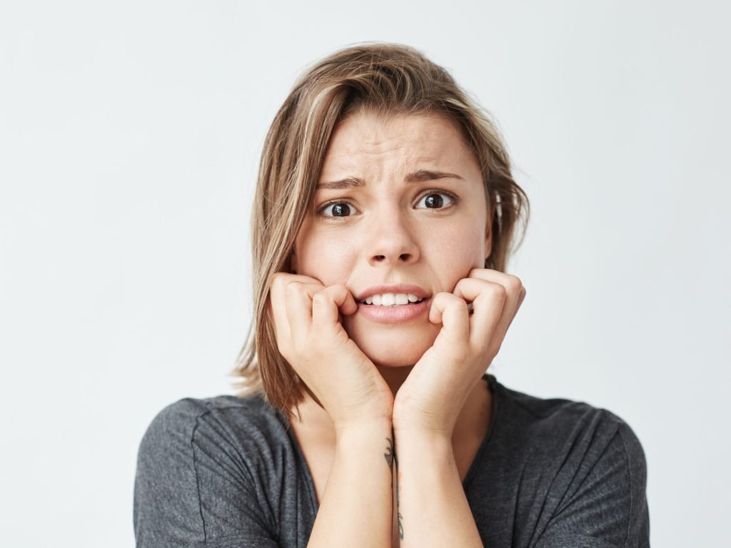 Nervous young beautiful girl looking at camera holding hands on cheeks over white background. Copy space.