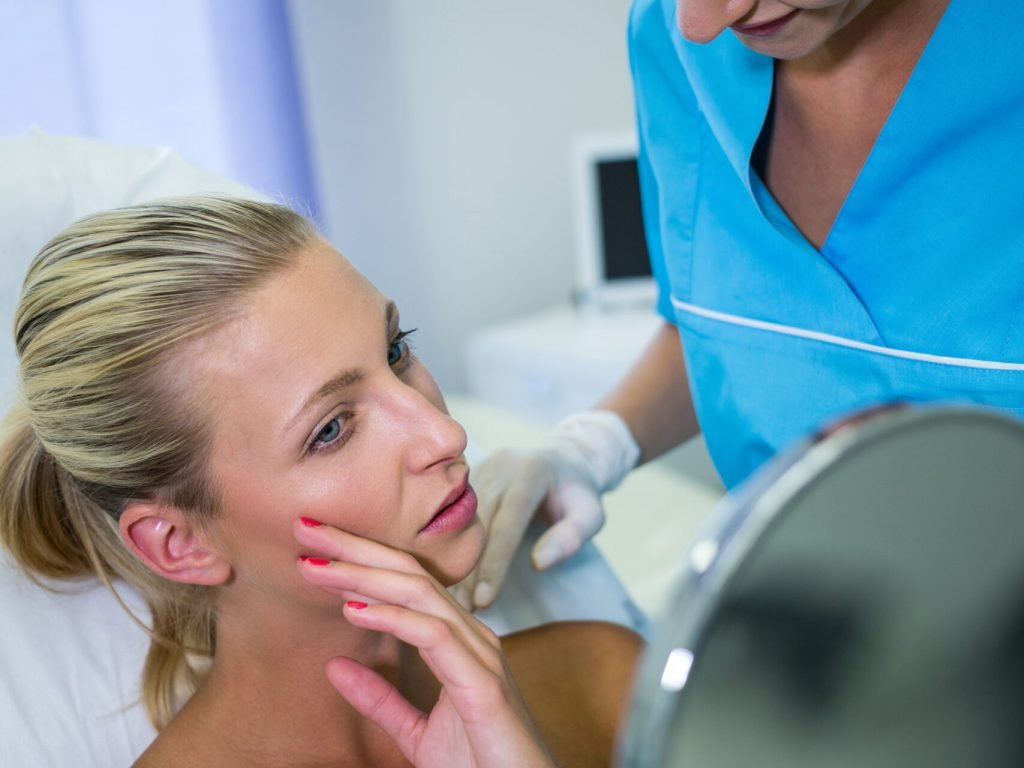 Happy woman checking her skin in the mirror after receiving cosmetic treatment
